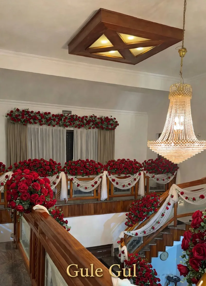 Red Rose Balcony and Stair Decor: Red roses along a balcony and stair railing with white drapes and a rose garland over the window, GuleGul Flowers Lahore