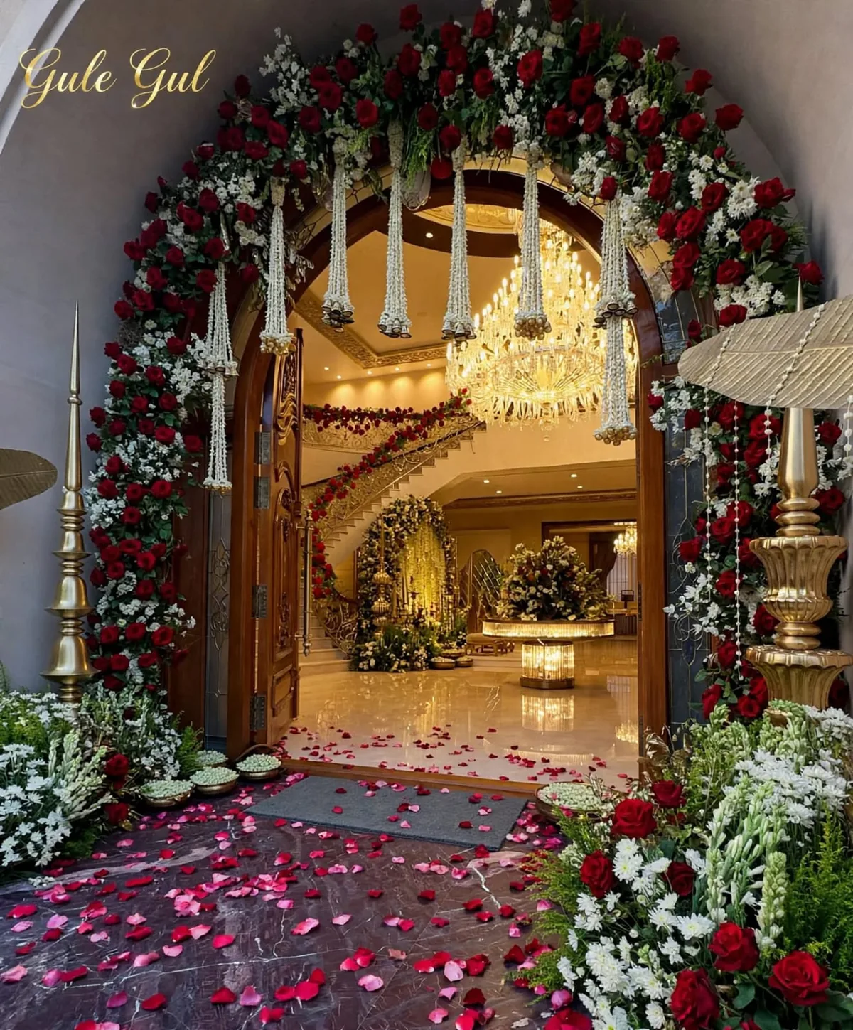 Rose and Motia Entrance Arch: Red and white rose arch over a main door with hanging white flower strings and rose petals on the floor, GuleGul Flowers Lahore
